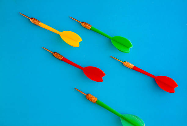 Multicolored red yellow green darts arrows on yellow violet blue background. Flat lay. View from above. Copy space. The concept of hitting the target, dedication.