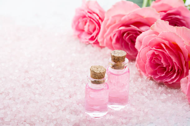 two bottles with rose oil, spa salt crystals and pink roses. - rose colored imagens e fotografias de stock