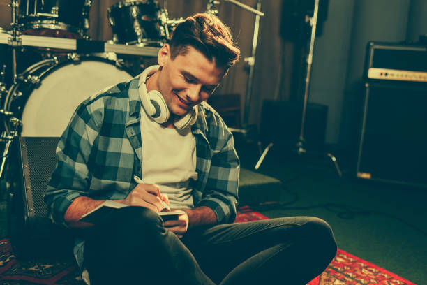 istock cheerful composer in headphones writing in notebook while sitting near drums 1160726992
