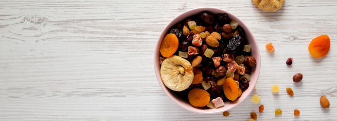 Dried fruits and nut mix in a pink bowl on a white wooden surface, top view. Overhead, from above, flat lay. Copy space.