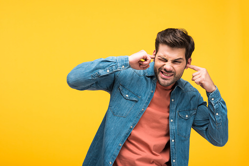 dissatisfied handsome man plugging ears with fingers Isolated On yellow