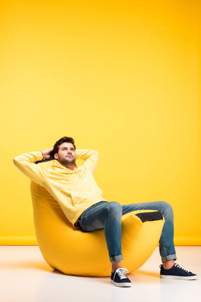 istock man with Hands Behind Back relaxing on bean bag chair on yellow 1160729815