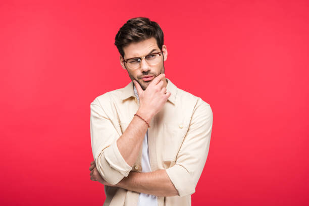 pensive man in glasses touching chin isolated on pink