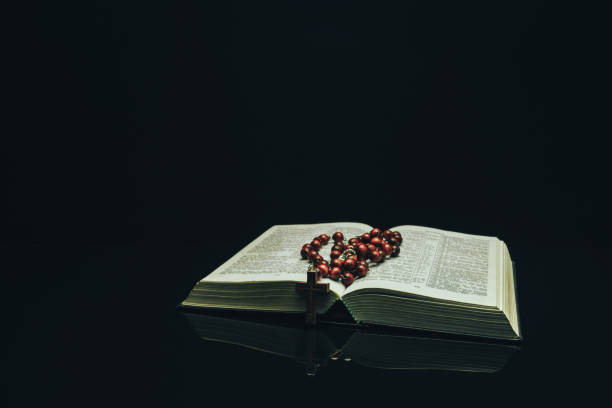 istock Open Holy Bible and beads on a black glass table dark background 1160733538
