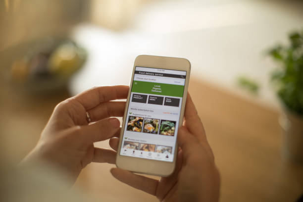 Woman using meal delivery service through mobile app. Woman is using mobile phone to order healthy organic veggies. She want to prepare healthy meal kitchen counter photos stock pictures, royalty-free photos & images