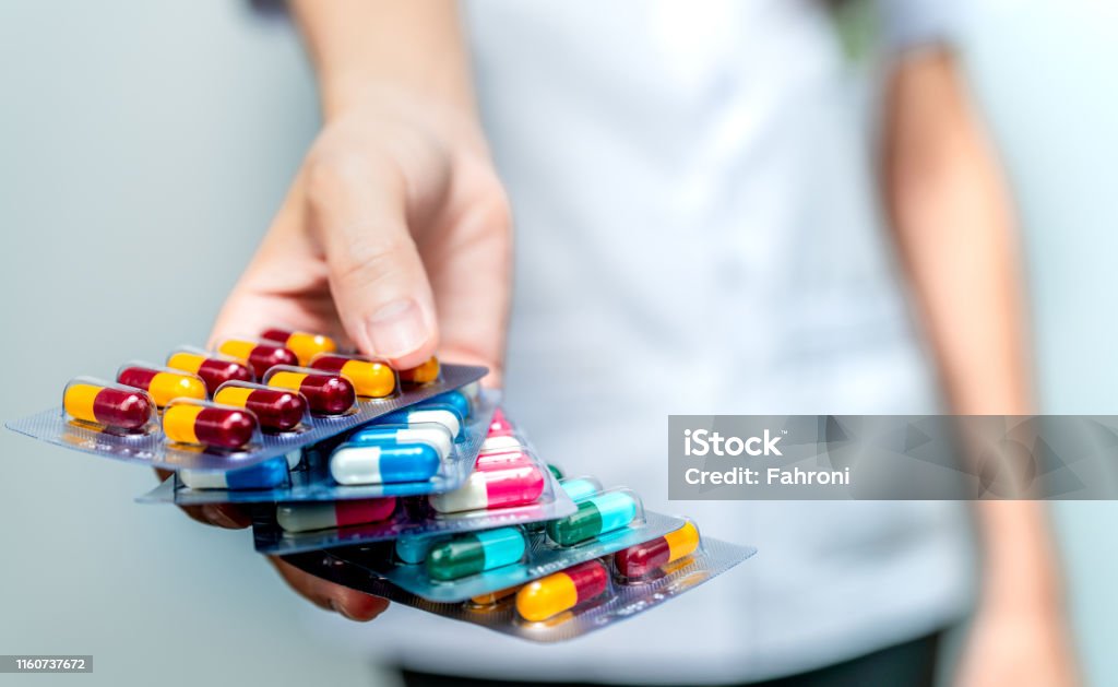 Pharmacist or doctor hand holding pack of antibiotic capsule pills and giving patient or people. Antibiotic drug overuse. Antimicrobial drug resistance. Community pharmacist. Drugstore background. Medicine Stock Photo