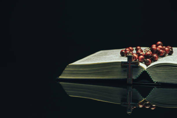 istock Open Holy Bible and beads on a black glass table dark background 1160738410