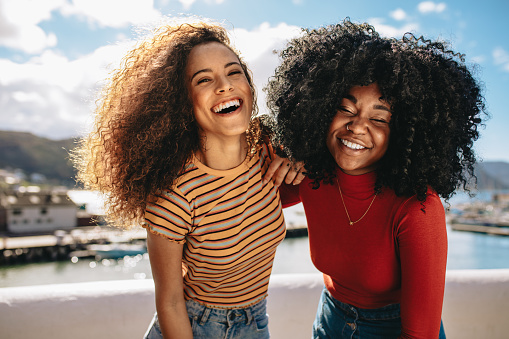 Two beautiful young women enjoying on the beach. Female friends walking on the beach and laughing on a summer day.