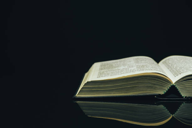 istock Open Holy Bible on a black glass table dark background 1160739887