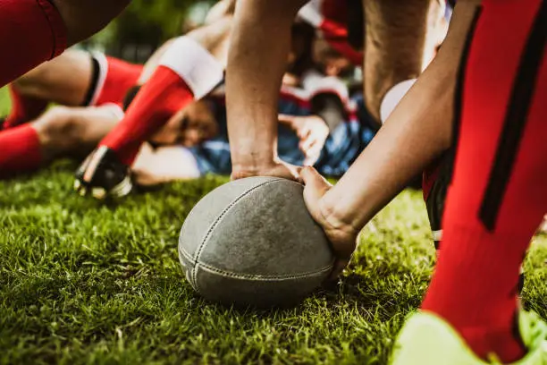 Close up of unrecognizable rugby player holding a ball on grass during a match at playing field.