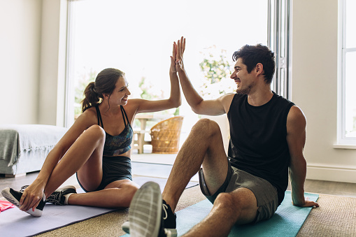 Couple giving each other high five after a successful workout together. Man and woman in sports wear doing workout in living room.