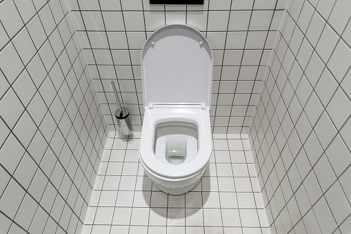 New clean toilet, with modern design and white ceramic toilet bowl against light tiles.