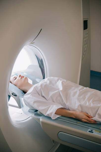 женщина с закрытыми глазами, лежащими на компьютере томограф стол во время радиологического теста - томография стоковые фото и изображения