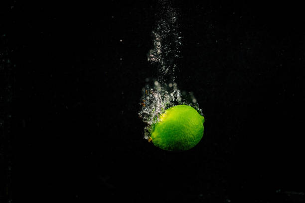 istock Sparkling green lime splashes water on black background 1160762836
