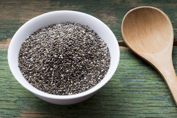 Top view of chia seeds in white bowl with wooden spoon, healthy superfood or ingredient stock photo