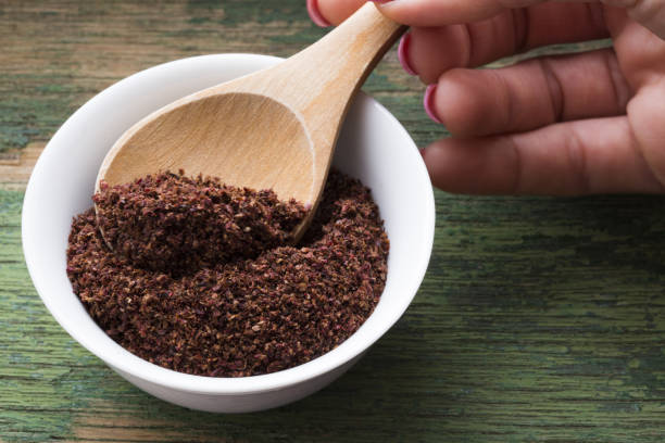 Woman taking sumac spice with wooden spoon from white bowl stock photo