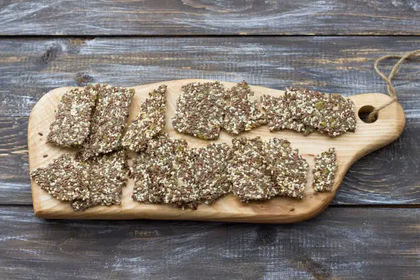 Delicious healthy multigrain gluten-free crackers, ketogenic, from chia seeds, flax, sesame and ground pumpkin seeds on a wooden board and on a wooden table with free space, top view, horizontal