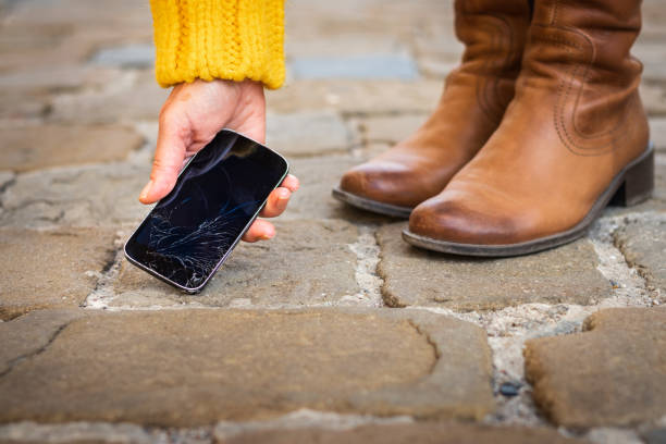 mujer recogiendo teléfono inteligente roto de la acera. teléfono celular dañado - dropped call fotografías e imágenes de stock