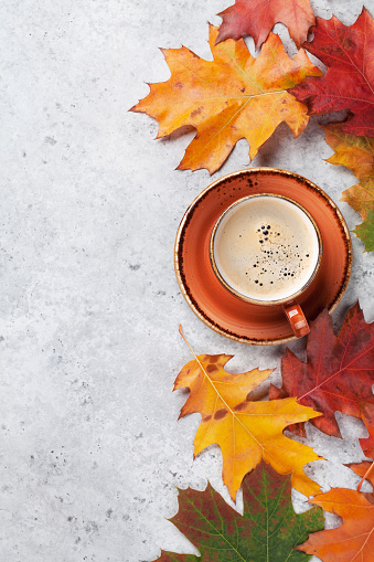 Autumn backdrop with colorful leaves over stone background and coffee cup. Top view with space for your text