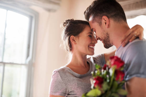 Always treat your lady special Shot of a young man surprising his girlfriend with a bunch of roses in their bedroom at home falling in love stock pictures, royalty-free photos & images