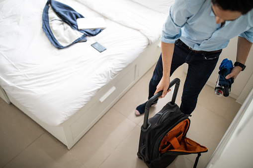Unrecognizable businessman folding clothes inside of luggage in the bedroom for business trip