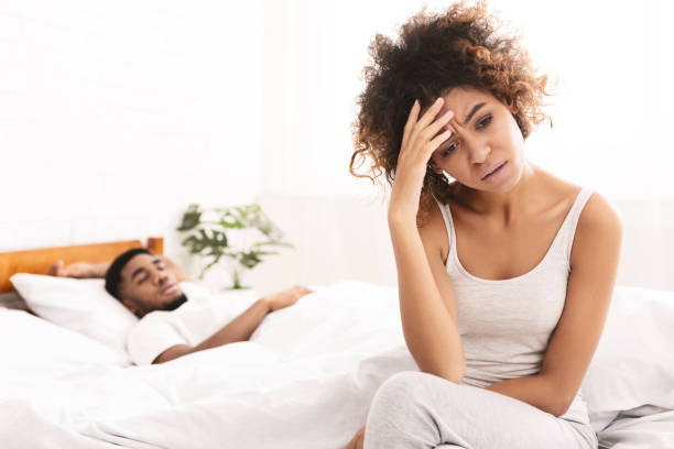 mujer negra infeliz que sufre de dolor de cabeza, sentada en la cama - couple love snoring sleeping fotografías e imágenes de stock