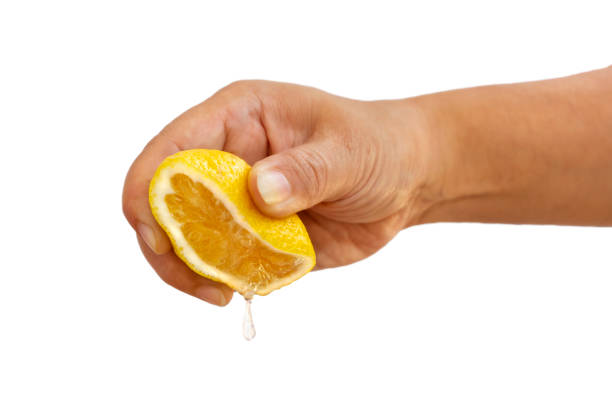manos de mujer apretando la mitad de amarillo limón fresco sobre un fondo blanco. - freshly squeezed fotografías e imágenes de stock