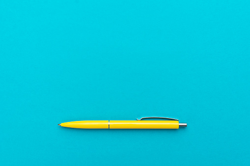 top view of ballpoint pen on the blue background. minimalist flat lay photo of yellow pen over turquoise blue background with copy space