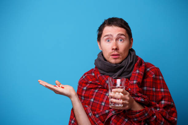 istock A wrapped in a blanket sick man with tablets and mug in his hands. 1160791408