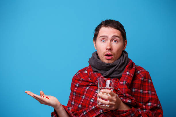 istock A wrapped in a blanket sick man with tablets and mug in his hands. 1160792396