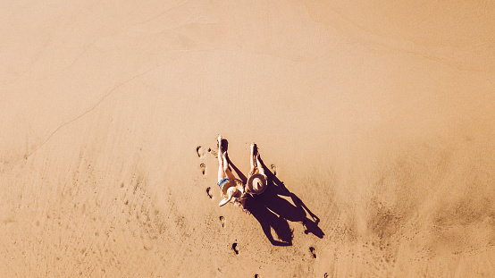 People enjoying vacation at the beach in resort hotel viewed  from vertical aerial pov - couple of girls sit down on the sand for summer holiday - tourists outdoor from above - scenic concept