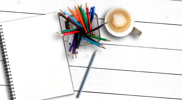 top view of box filled with colored pencils and sketchbook or spiral notepad on rustic white wooden table