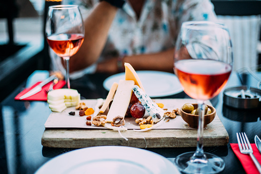 wo glasses of rose wine and board with fruits, bread and cheese on wooden table