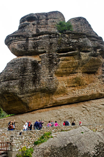 Tourists walk in front of a giant rock while walking toward the Monastery of Varlaam in Meteroa. The unique rock formations are a popular tourist destination as they contain caves and monasteries on the cliff edges. Meteora is a UNESCO World Heritage Site.
