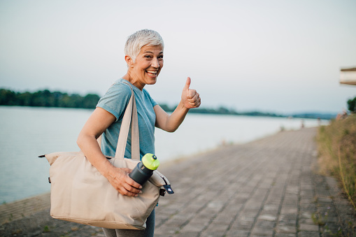 Woman with bottle of water going home after outdoor run and pointing thumb up