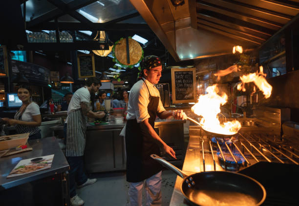 chef cooking at a restaurant flaming the food - commercial kitchen restaurant chef food service occupation imagens e fotografias de stock