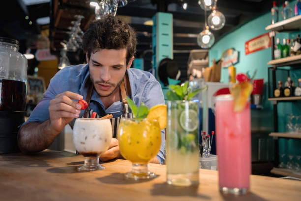 Bartender decorating beautiful cocktails at the bar with strawberries - food and drinks concepts