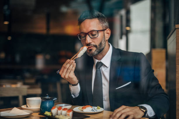 uomo che mangia sushi al ristorante - sushi chopsticks sushi bar food foto e immagini stock