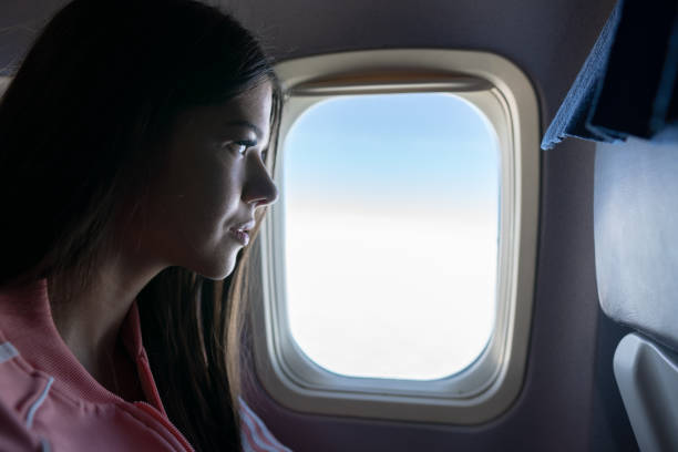 istock Young woman looking through window in airplane 1160830608