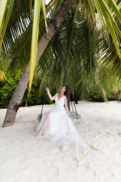 istock A bride in a white dress is riding on a swing under a big palm tree. 1160835121