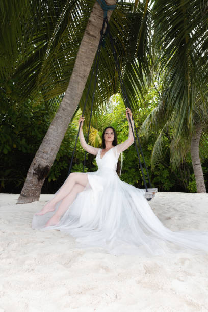 istock A bride in a white dress is riding on a swing under a big palm tree. 1160835175