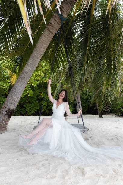 istock A bride in a white dress is riding on a swing under a big palm tree. 1160835179