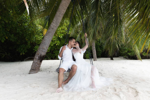 istock Newlyweds kiss on a swing under a big palm tree. 1160835180