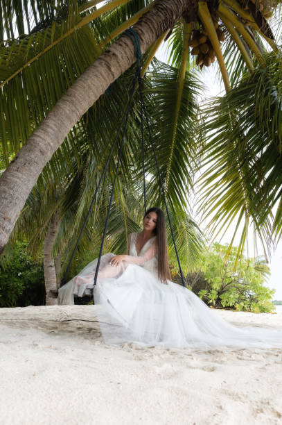 istock A bride in a white dress is riding on a swing under a big palm tree. 1160835181