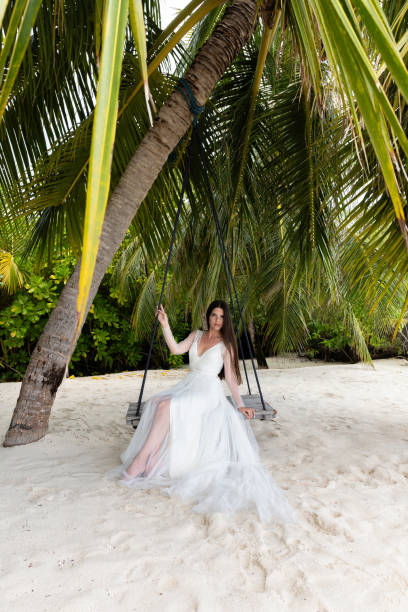 istock A bride in a white dress is riding on a swing under a big palm tree. 1160835184