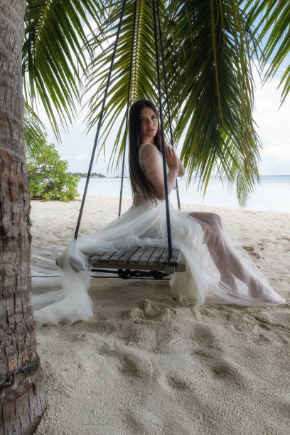 istock A bride in a white dress is riding on a swing under a big palm tree. 1160835198
