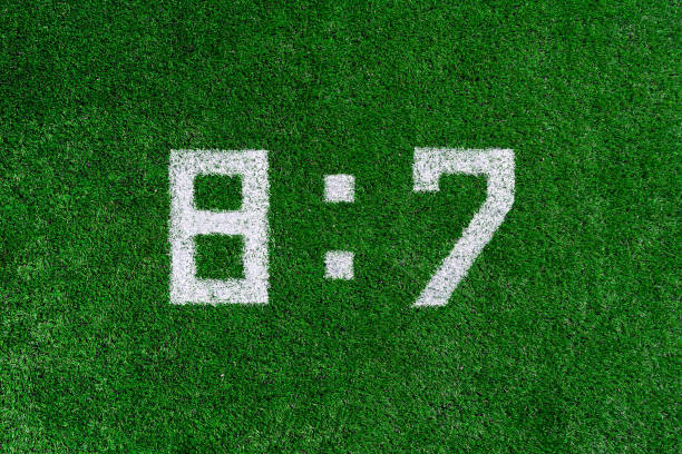 istock Football score 8:7.White numbers eight and seven are drawn on the green grass,creative scoreboard 1160841641