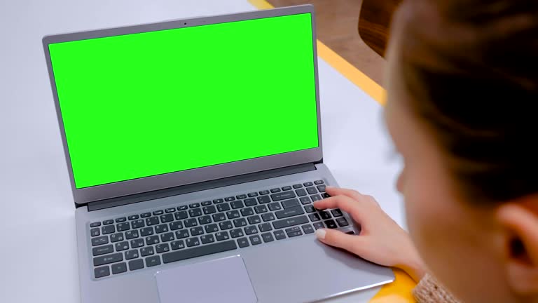 Woman looking at laptop computer with blank green screen in cafe