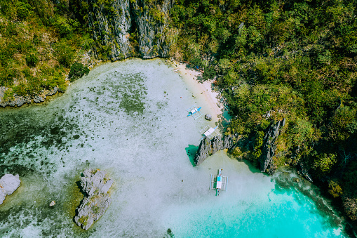 Aerial drone view of filippino tourist banca boats in shallow blue turquoise water in Ubugon Cadlao lagoon surrounded by karst cliffs. El Nido, Palawan island, Philippines.