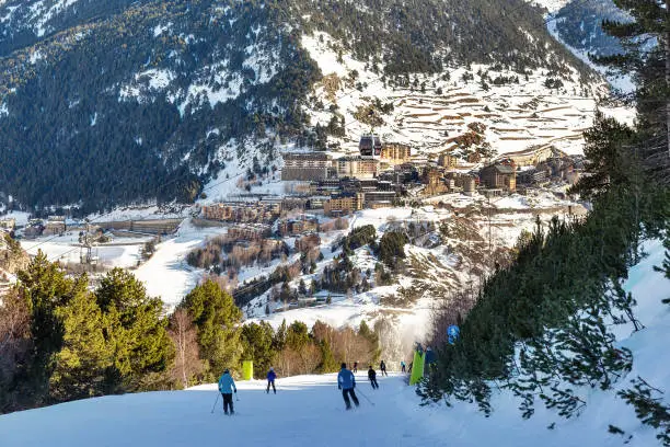 View of the village in the Pyrenees, Andorra from the ski slopes in winter. traditional houses on the mountainside and descending skiers in the foreground